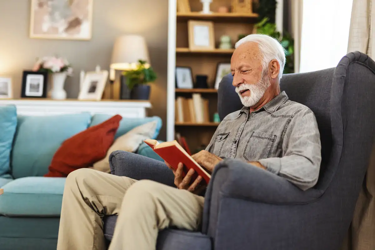 Senior man reading a book at home, thinking about when to move to independent living.